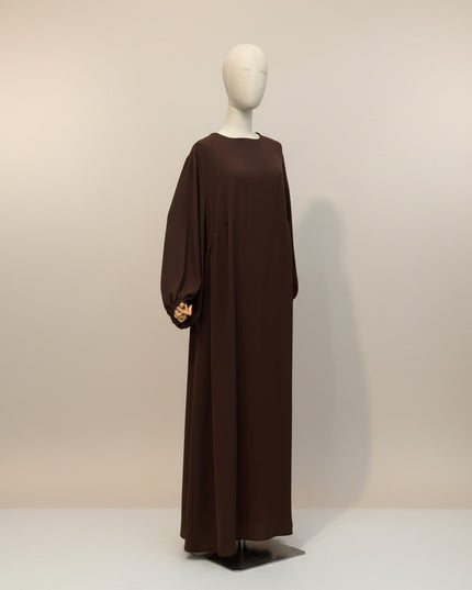 Awra.at Abaya Kamila, a long, dark brown, modest dress with voluminous balloon sleeves and a crew neck, displayed on a mannequin.